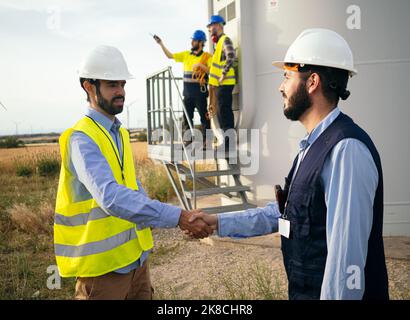 Two male engineers shake hands in a field of windmills. Agreement, renewable energy, energy transition Stock Photo