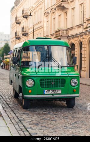 Confident, middle-aged, bearded, grey-haired man in a blazer and a turtleneck with glasses on, standing with his arms crossed in front of an old green minibus. High quality photo Stock Photo
