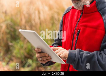Unknown, caucasian, bearded, mature man, professional construction worker in uniform standing, using an electronic tablet for work, checking information. Hands close up. High quality photo Stock Photo