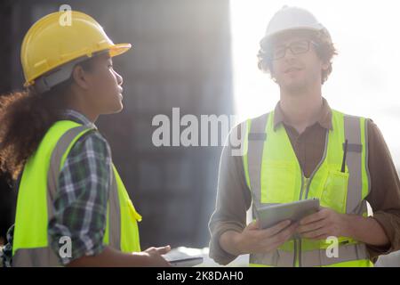 Young man and woman is architect planning and inspector project and looking digital tablet at construction site, engineer male and female working and Stock Photo