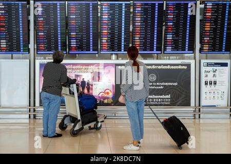 Bangkok, Thailand - October 26, 2022 : asian woman passenger with luggage looking departure timetable board to checking flight at suvarnabhumi airport Stock Photo
