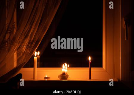 Candles on the window in an apartment in Ukraine, Ukraine without electricity due to the war, an apartment without light, the light of a candle in the Stock Photo