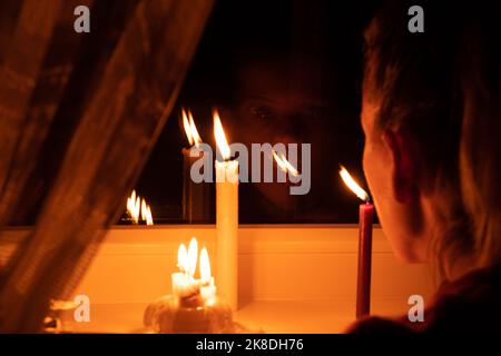 The girl's face put candles on the window in an apartment in Ukraine, Ukraine without electricity because of the war, an apartment without light Stock Photo