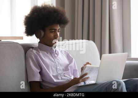 Attentive African student guy in headphones studying online using laptop Stock Photo
