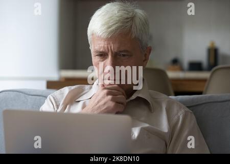 Thoughtful grey-haired mature man learning laptop app or software Stock Photo