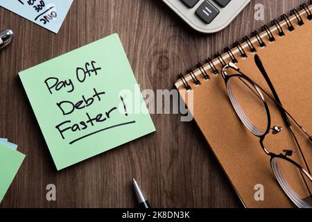 Sticky note with pay off debt faster! message on a wooden desk with office items Stock Photo