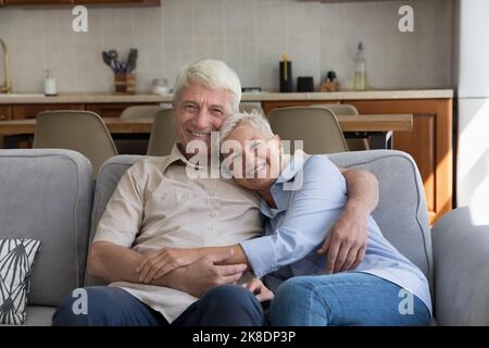 Loving older couple hugging relaxing on sofa looking at camera Stock Photo