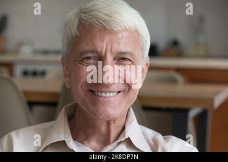 Happy older man sits indoors looking at camera Stock Photo