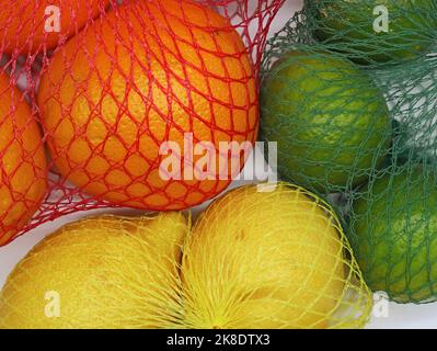 oranges, limes and lemons in plastic net bag, close up of citrus fruits in sales packaging Stock Photo
