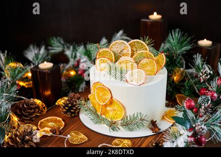 Christmas cake made of chocolate base with cream, decorated with dried orange slices against the backdrop of Christmas decor Stock Photo