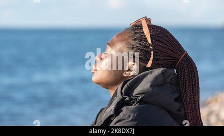 African woman sits by the Swedish Baltic Sea and enjoys the sunset Stock Photo