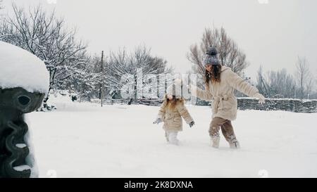 winter family activity outdoors. side view. Happy little girls, children are slowly walking through thick snow in the city park, during snowfall. family is having fun, spending time together on snowy winter day. slow motion. High quality photo Stock Photo