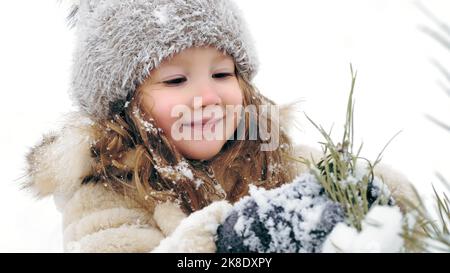 Christmas tree outdoor decoration. cutie, pretty little girl decorates snow-covered Christmas tree with homemade ice toys, during snowfall, in forest. happy time on snowy winter day. winter family activity outdoors. slow motion. High quality photo Stock Photo