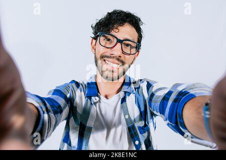 Handsome man taking a selfie looking at the camera on isolated background. Teenage guy taking a self portrait isolated. Guy with beard and glasses Stock Photo