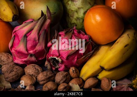 Close-up of tropical autumn fruits, pitahaya or dragon fruit surrounded by bananas, custard apples, persimmons, mango and dried fruits such. Stock Photo