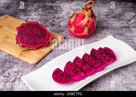 Pitaya or dragon fruit, half a pitahaya exposing the pink interior with black seeds and a plate with pieces of fruit ready to eat. Stock Photo