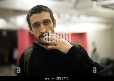 Guy keeps his fingers at his mouth. Young man in black jacket. Shingle. Serious look. Student at university. Stock Photo