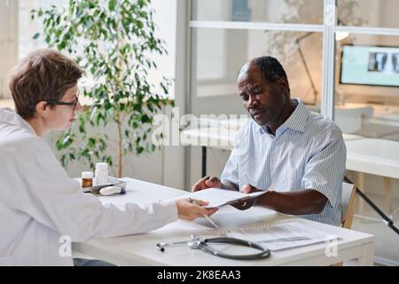 Female doctor showing diagnosis and giving prescription to patient while they sitting at table at office Stock Photo