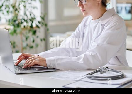 Close-up of female doctor using laptop at her online work while sitting at her workplace at office Stock Photo