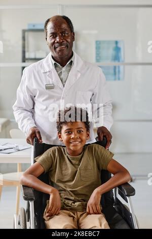 Portrait of African mature doctor with patient with disability standing at hospital and smiling at camera Stock Photo