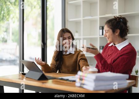 Two multiethnic professionals colleagues working together with laptop and papers in office. Female mentor and young professional sitting in creative Stock Photo
