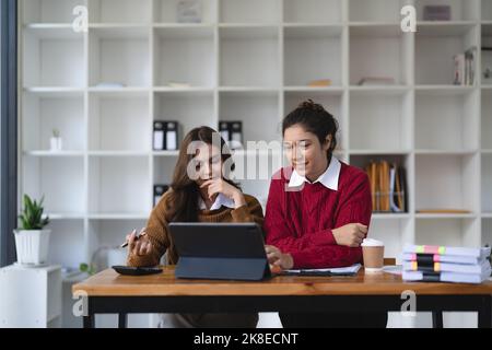 Two multiethnic professionals colleagues working together with laptop and papers in office. Female mentor and young professional sitting in creative Stock Photo