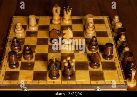 A beautiful vintage wooden chess board with some pieces on top and others beside it, on a wooden table Stock Photo