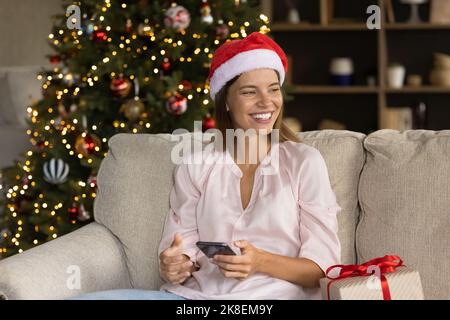 Relaxed dreamy young woman using cellphone, reading New Year congratulations. Stock Photo