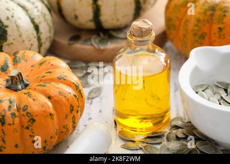 Pumpkin seeds oil bottle, pumpkins and mortar of seeds on wooden kitchen table. Stock Photo