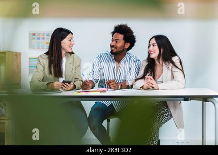 Three colleagues sitting and talking at table in office Stock Photo