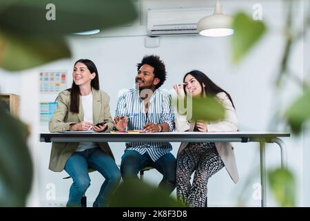 Three colleagues at table in office looking sideways Stock Photo