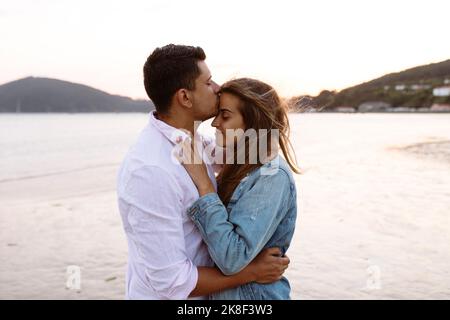 Young man kissing girlfriend's forehead at beach Stock Photo