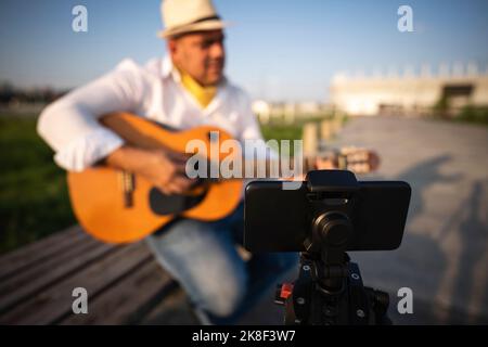 Street musician playing guitar and recording through smart phone on tripod Stock Photo