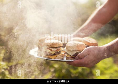 Hand's of man serving cheeseburgers amidst smoke at backyard Stock Photo
