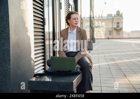Thoughtful young freelancer with laptop sitting on bench Stock Photo