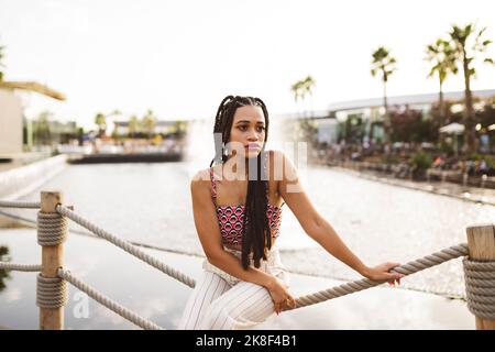 Thoughtful young woman sitting on rope fence Stock Photo