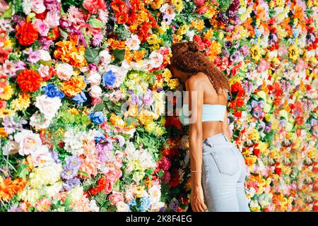 Young curly hair woman leaning head on flower wall Stock Photo