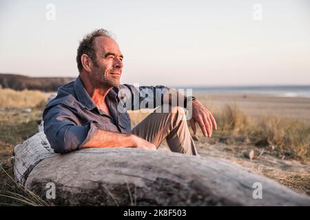 Mature man leaning on log enjoying sunset Stock Photo