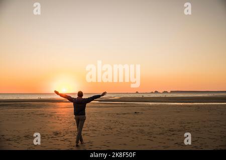 Man with arms outstretched enjoying on shore at sunset Stock Photo