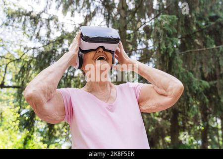Happy senior woman watching through VR Goggles in park Stock Photo