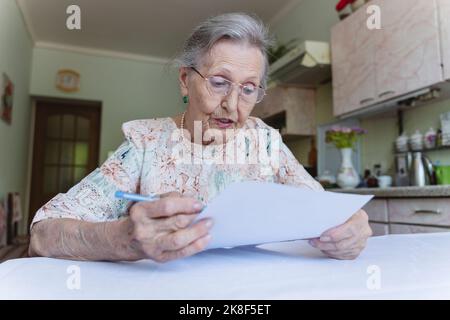 Senior woman reading contract at table in home Stock Photo