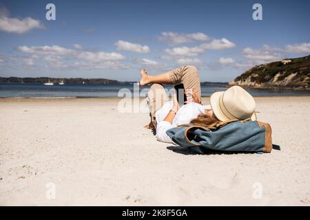 Woman with backpack using smart phone lying at beach Stock Photo