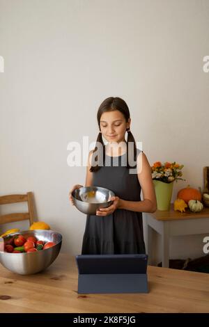 Smiling girl holding steel bowl with tablet PC on table at home Stock Photo