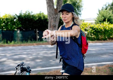 Senior woman on bicycle checking time in smart watch Stock Photo
