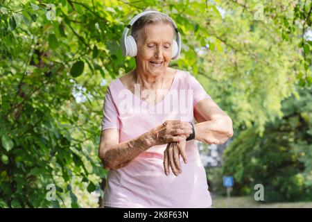 Smiling senior woman with smart watch listening to music through headphones in park Stock Photo