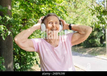 Happy senior woman wearing wireless headphones exercising in front of tree Stock Photo