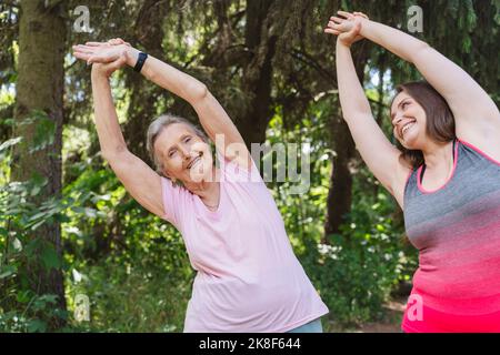 Happy fitness instructor with senior woman practicing stretching exercise at park Stock Photo