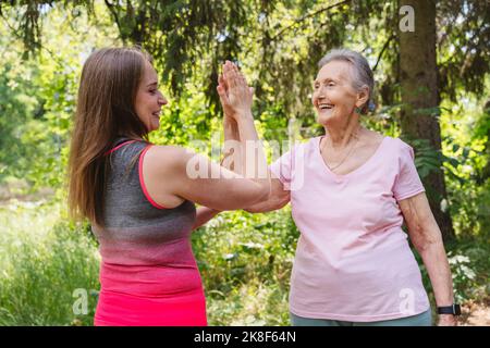 Smiling fitness instructor touching hand of senior woman exercising at park Stock Photo