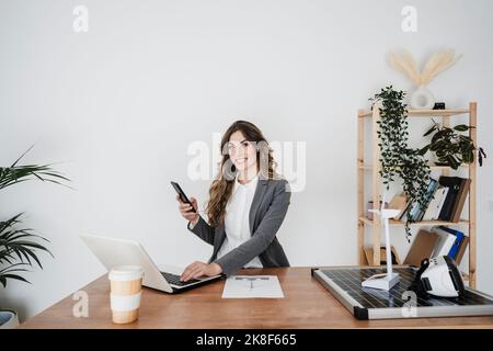 Young female engineer working in modern office sitting at desk using smartphone Stock Photo