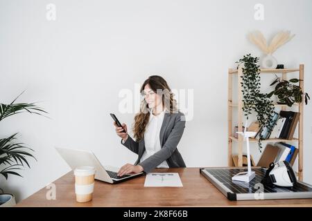 Young female engineer working in modern office sitting at desk using smartphone Stock Photo